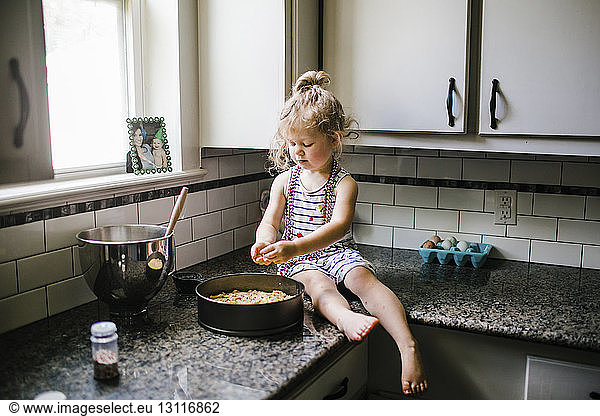 Girl preparing food in container while sitting on kitchen counter