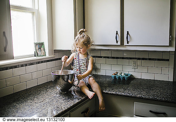 Girl preparing food in container while sitting on kitchen counter at home