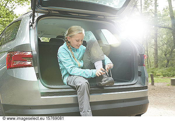 Girl preparing for hike at back of car tying shoes