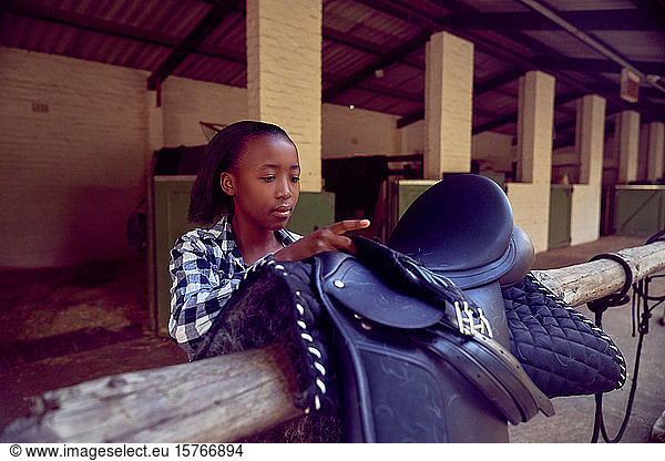 Girl preparing saddle for horseback riding outside stables