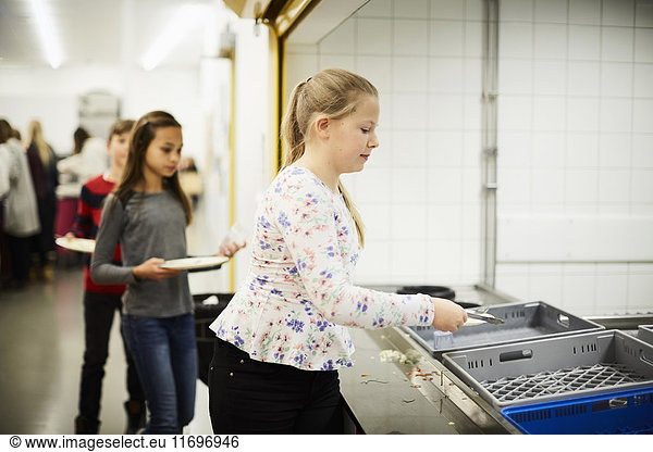 Girl putting plate in crate after having lunch at school cafeteria