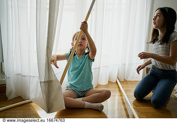 Girl putting the sticks to build a teepee tent inside their house. Creativity concept