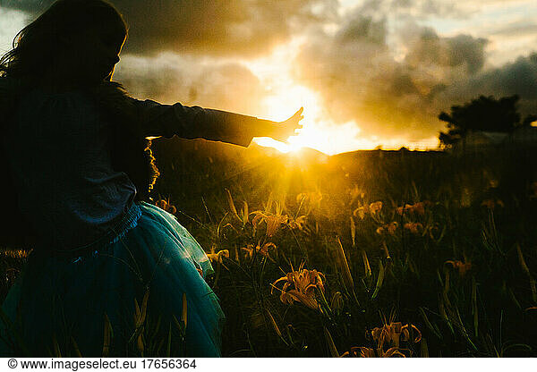 Girl reaches hand toward sunrays in flower field