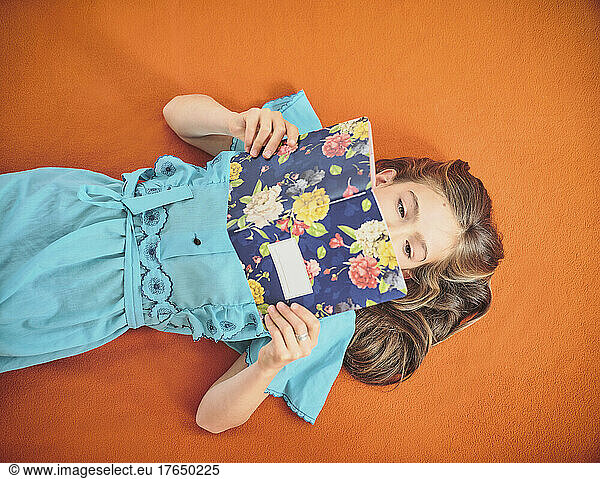 Girl reading book lying on orange background