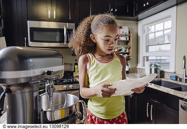 Girl reading recipe while baking in kitchen