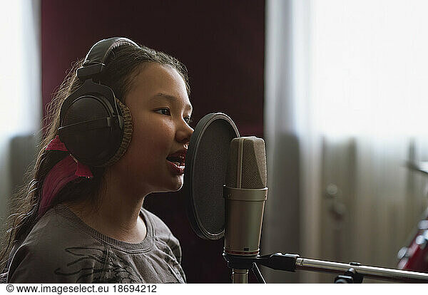 Girl recording song on microphone in studio
