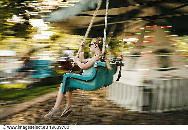 Girl rides chair swings at amusement park on a warm day