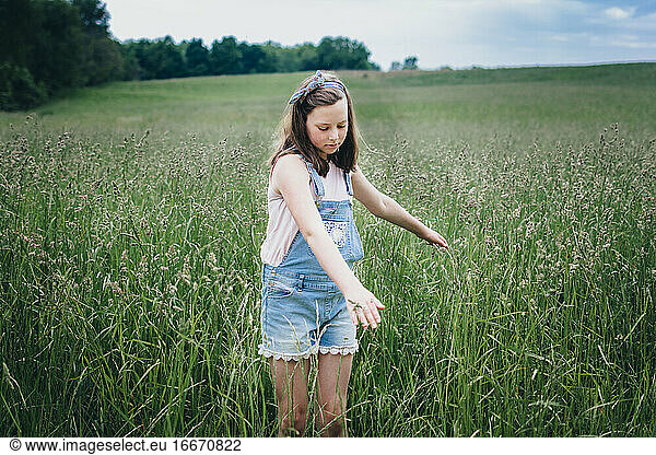 Girl Running her Hands Through Tall Grass in a Field in the Midwest
