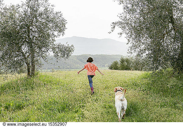 Girl running with labrador dog in scenic field landscape  rear view  Citta della Pieve  Umbria  Italy