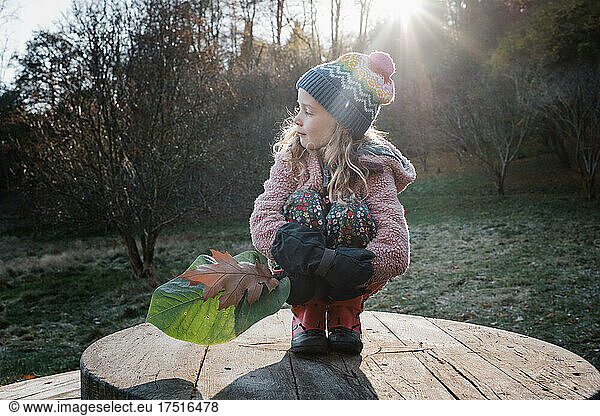 girl sat with leaves in the forest in Autumn at sunset
