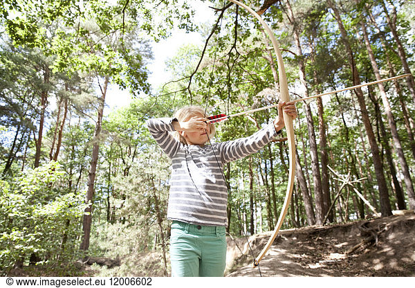 Girl shooting with bow and arrow in the forest