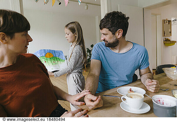 Girl showing painting to father and mother having breakfast at home
