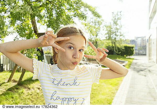 Girl showing peace sign standing in front of tree