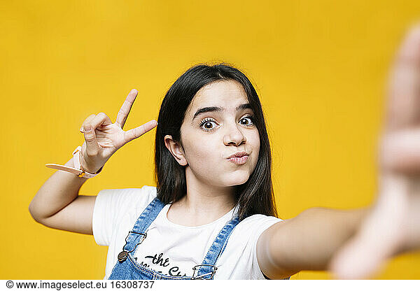 Girl showing peace sign while standing against yellow background