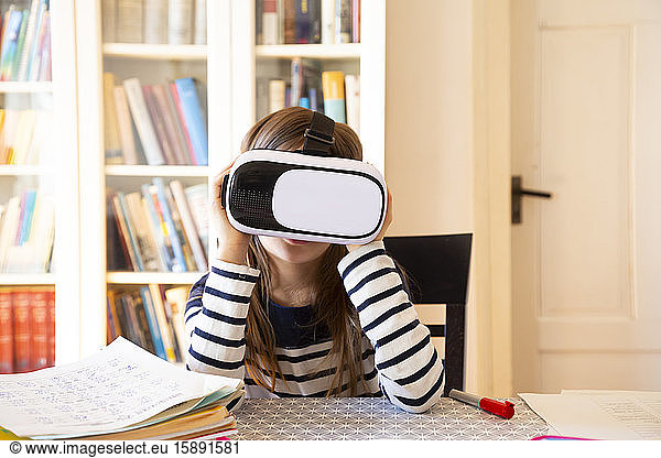 Girl sitting at table at home using virtual reality glasses