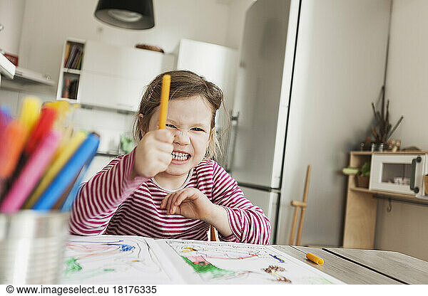 Girl Sitting at Table Colouring Pictures and Pointing Marker to the Camera