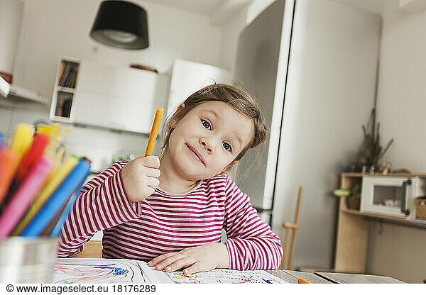 Girl sitting at Table Colouring Pictures and Smiling at Camera