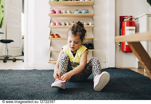 Girl sitting on carpet wearing shoes against rack in cloakroom at child care