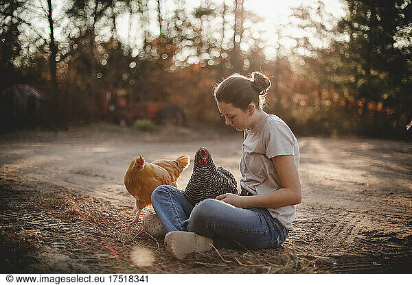 Girl sitting on dirt driveway with chickens