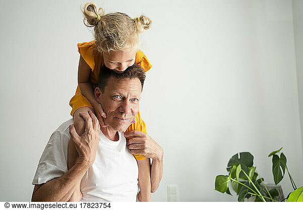 Girl sitting on father's shoulders at home