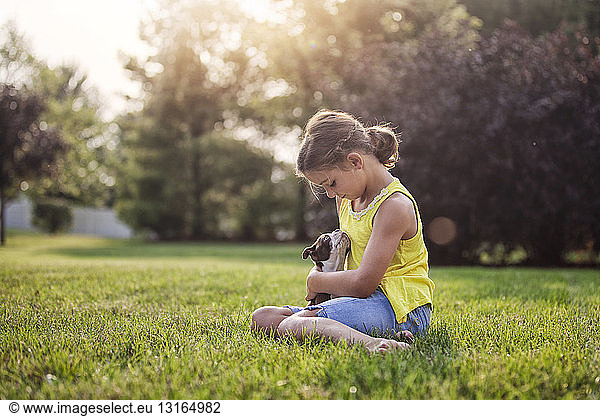 Girl sitting on grass holding Boston Terrier puppy