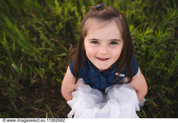 Girl sitting on grass looking up at camera smiling