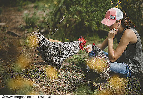 Girl sitting on ground with rooster and hen