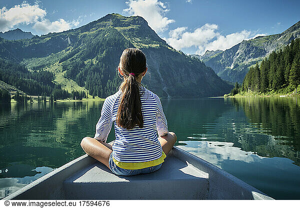 Girl sitting on prow of rowboat and admiring mountains