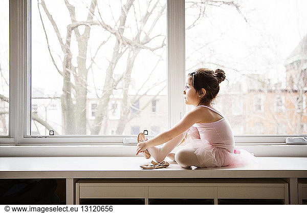 Girl sitting on table and wearing ballet shoes against window