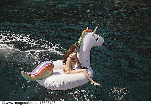 Girl sitting on unicorn air mattress in sea at vacation