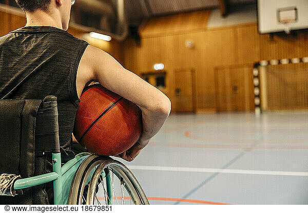 Girl sitting on wheelchair holding basketball at sports court
