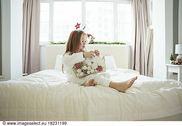 Girl sitting with basket of Christmas baubles on bed at home