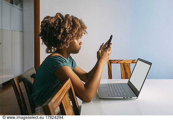 Girl sitting with laptop using smart phone at home