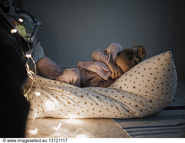 Girl sleeping by illuminated string lights on bed at home