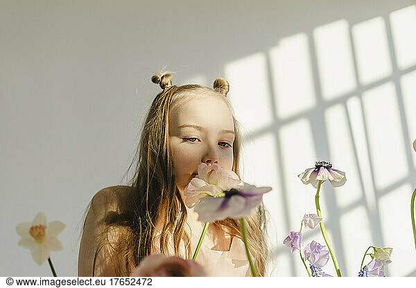 Girl smelling fresh flowers in front of white wall