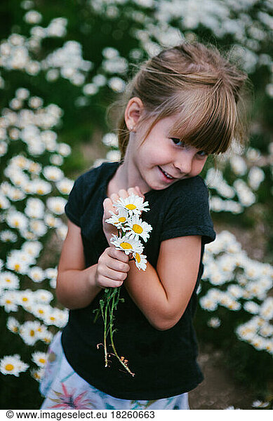 Girl smiles with white and yellow daisies in daisy flower field