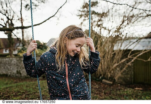 girl smiling on a swing in her backyard at sunset