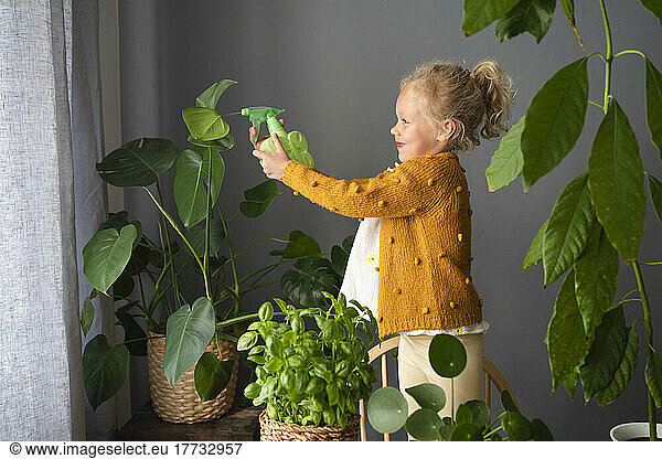 Girl spraying water on potted plants at home