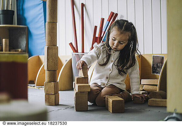 Girl stacking toy blocks while sitting in kindergarten