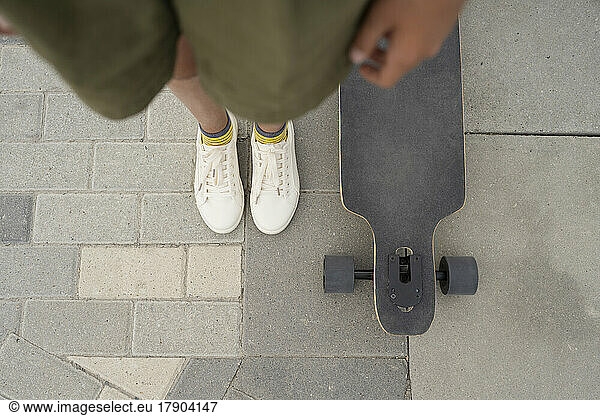 Girl standing by skateboard on footpath