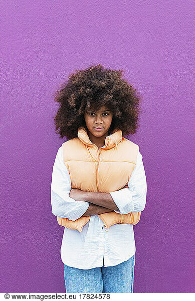 Girl standing with arms crossed against purple background