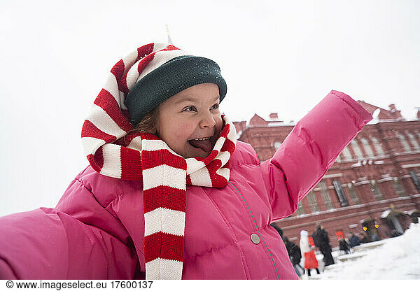 Girl standing with arms outstretched sticking out tongue in winter