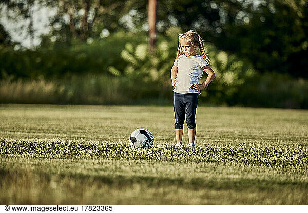 Girl standing with hand on hip by soccer ball at sports field