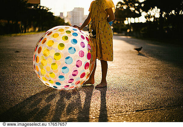 Girl stands in golden light with rainbow ball in yellow dress