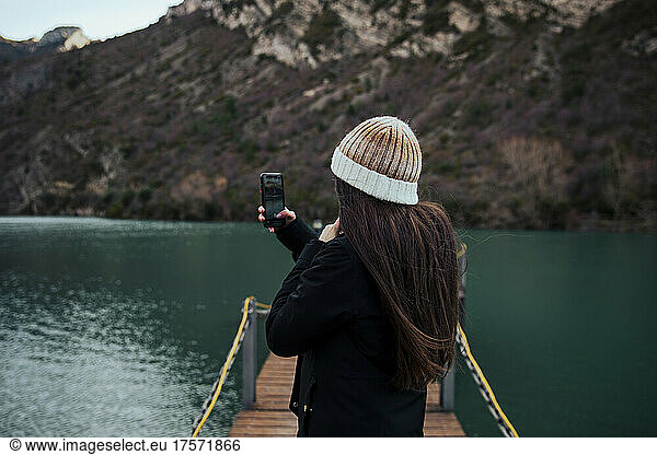 Girl taking a photo with her mobile on a lake pier