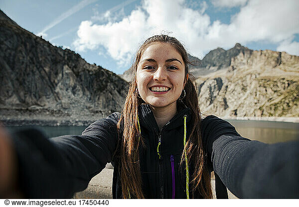 Girl taking a selfie while smiling with a lake in the background