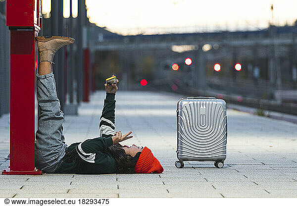 Girl talking selfie through smart phone lying down at train platform