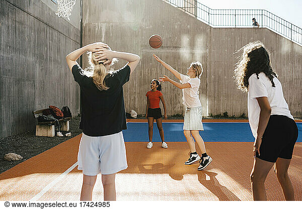 Girl throwing basketball towards hoop while playing with friends at court