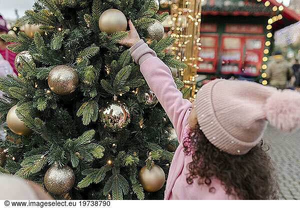 Girl touching Christmas ornament on tree at market