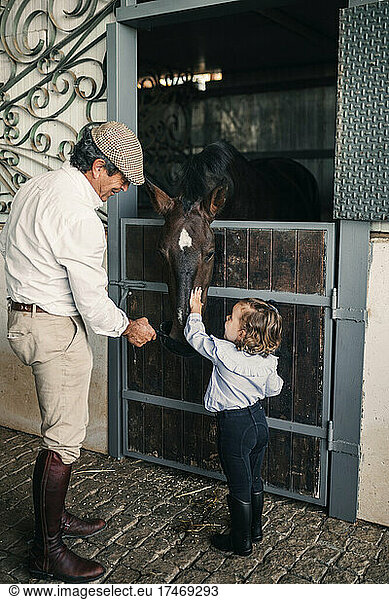Girl touching horse while standing by grandfather at stable